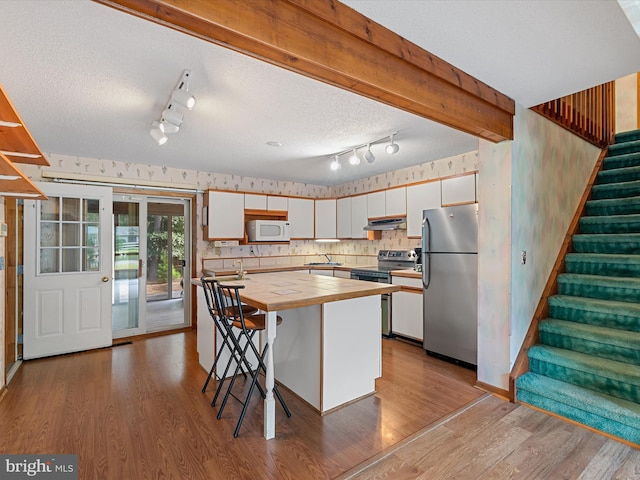 kitchen featuring wood counters, wood-type flooring, beam ceiling, stainless steel appliances, and white cabinets