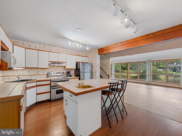 kitchen with appliances with stainless steel finishes, white cabinetry, an island with sink, and a textured ceiling