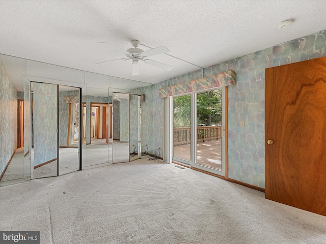 unfurnished bedroom with a textured ceiling, carpet flooring, ceiling fan, and multiple closets