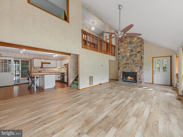 unfurnished living room with a fireplace, french doors, high vaulted ceiling, ceiling fan, and light wood-type flooring