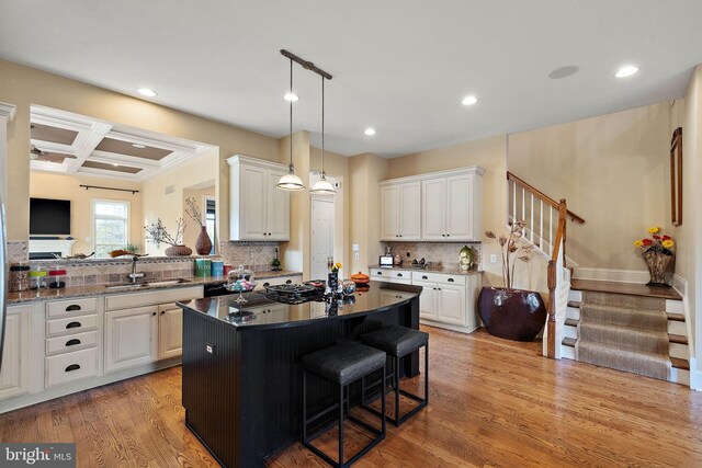 kitchen with coffered ceiling, a kitchen island, backsplash, and light hardwood / wood-style floors