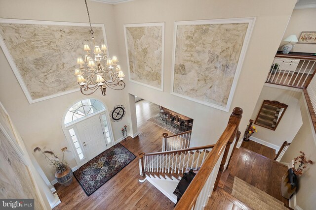 foyer with a towering ceiling, crown molding, wood-type flooring, and an inviting chandelier