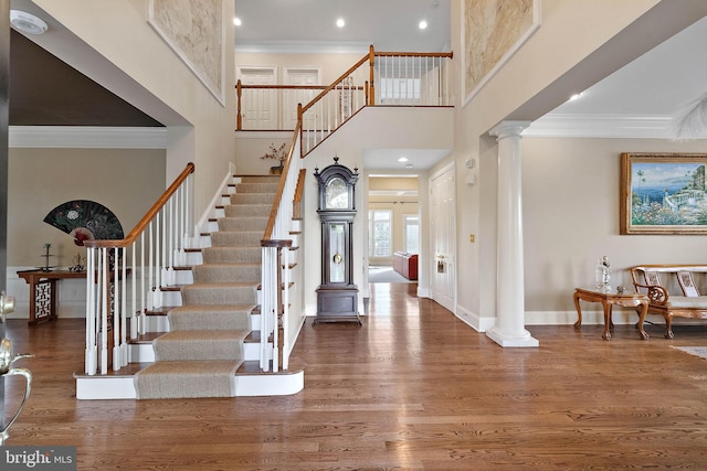 entrance foyer with ornamental molding, a towering ceiling, hardwood / wood-style floors, and decorative columns