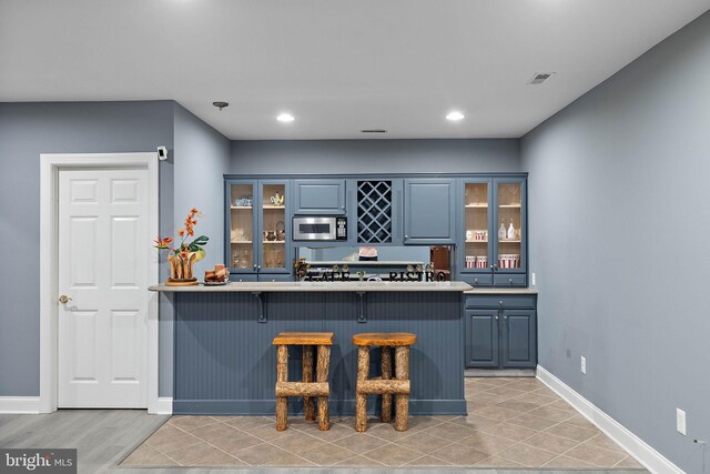 kitchen featuring light wood-type flooring, stainless steel microwave, kitchen peninsula, and a kitchen bar