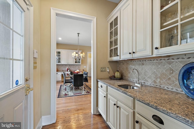 kitchen with an inviting chandelier, hardwood / wood-style floors, sink, decorative backsplash, and white cabinets