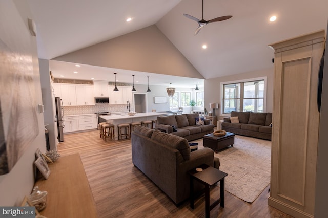 living room with high vaulted ceiling, light hardwood / wood-style flooring, sink, and ceiling fan