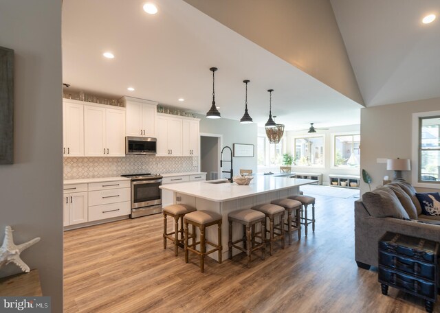 kitchen with vaulted ceiling, white cabinetry, stainless steel appliances, and a center island with sink