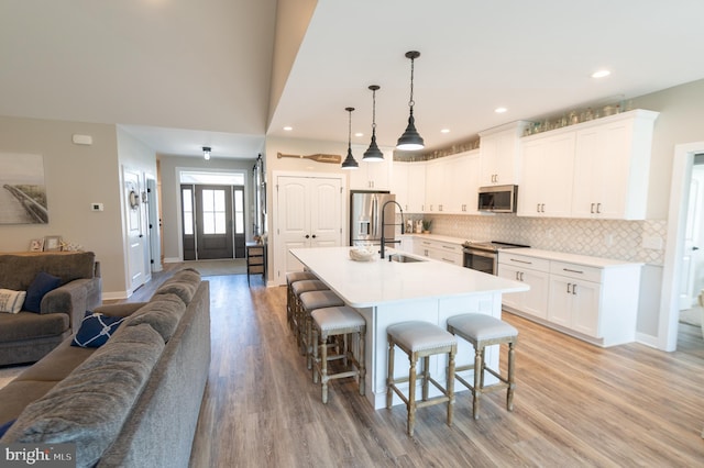 kitchen with stainless steel appliances, a breakfast bar area, white cabinetry, and light hardwood / wood-style floors