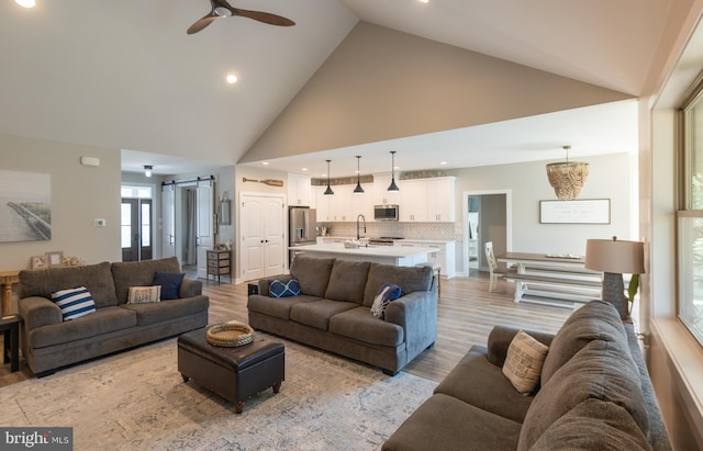 living room featuring light hardwood / wood-style floors, sink, high vaulted ceiling, a barn door, and ceiling fan