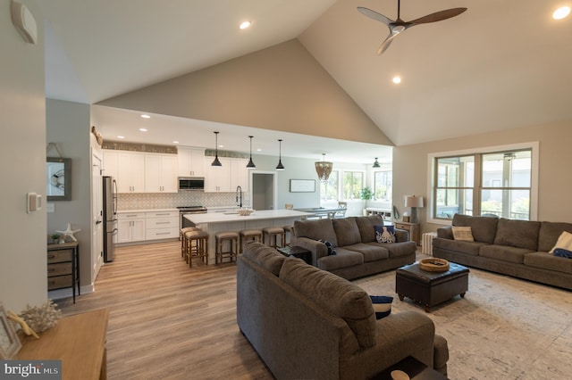 living room with light hardwood / wood-style flooring, ceiling fan, sink, and high vaulted ceiling