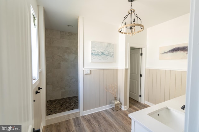 bathroom with an inviting chandelier, hardwood / wood-style floors, a tile shower, sink, and wooden walls