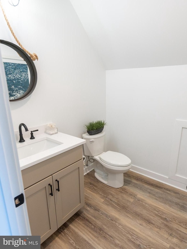 bathroom featuring wood-type flooring, toilet, vaulted ceiling, and vanity