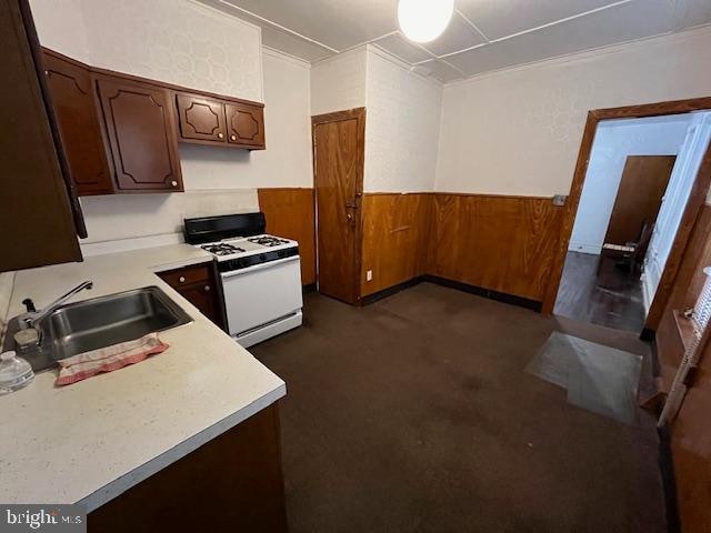 kitchen with white gas stove, crown molding, dark brown cabinets, and sink