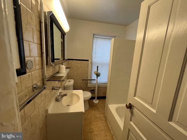 bathroom featuring a washtub, vanity, toilet, and tile walls