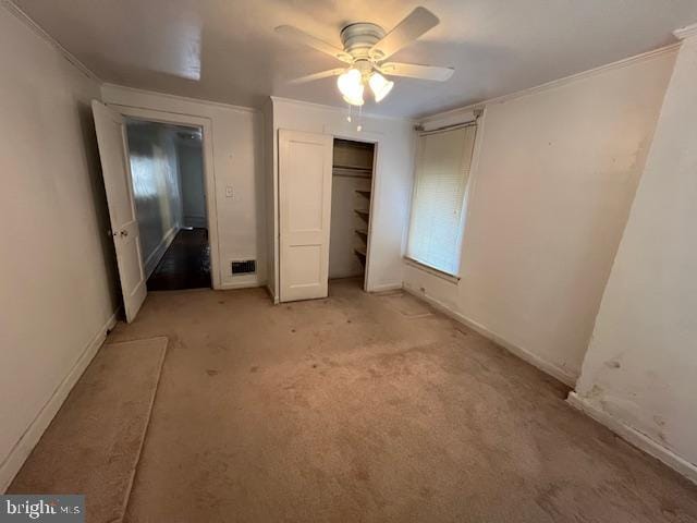 unfurnished bedroom with a closet, ceiling fan, crown molding, and light colored carpet