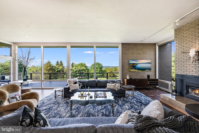 living room featuring hardwood / wood-style flooring, a fireplace, brick wall, rail lighting, and floor to ceiling windows