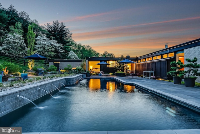 pool at dusk featuring a gazebo, a patio area, and pool water feature