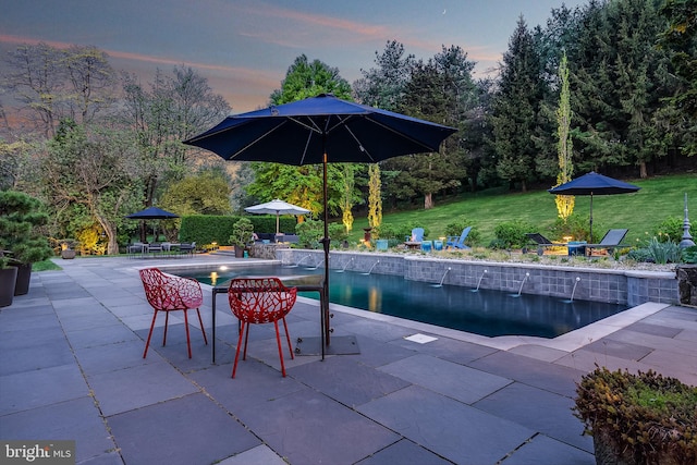 pool at dusk with a patio area and a lawn