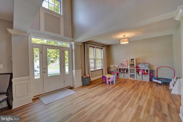 entryway featuring a high ceiling, light wood-type flooring, and ornate columns