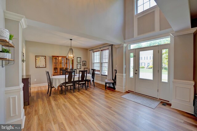 foyer with a towering ceiling, baseboards, visible vents, light wood-type flooring, and ornate columns