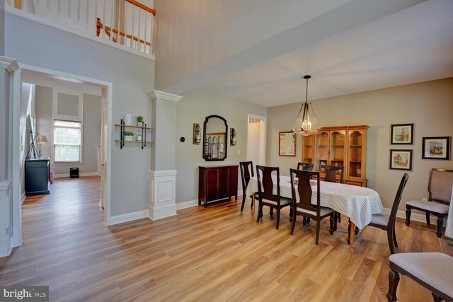 dining room with decorative columns, baseboards, a towering ceiling, light wood-style flooring, and a chandelier