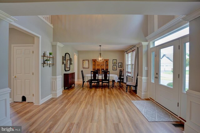 foyer entrance with light wood-type flooring, a decorative wall, wainscoting, and ornate columns