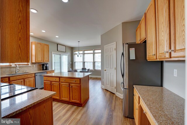 kitchen featuring stainless steel appliances, a sink, light wood-type flooring, backsplash, and a center island