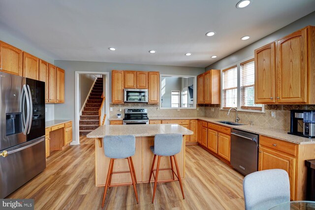 kitchen with light wood finished floors, appliances with stainless steel finishes, a kitchen bar, and a sink