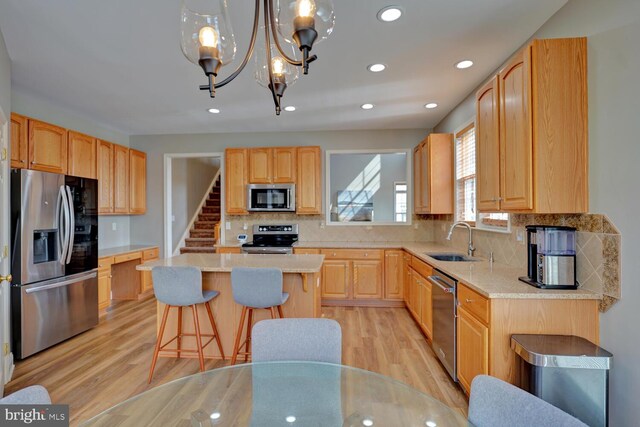 kitchen with a center island, a kitchen bar, stainless steel appliances, light brown cabinets, and a sink