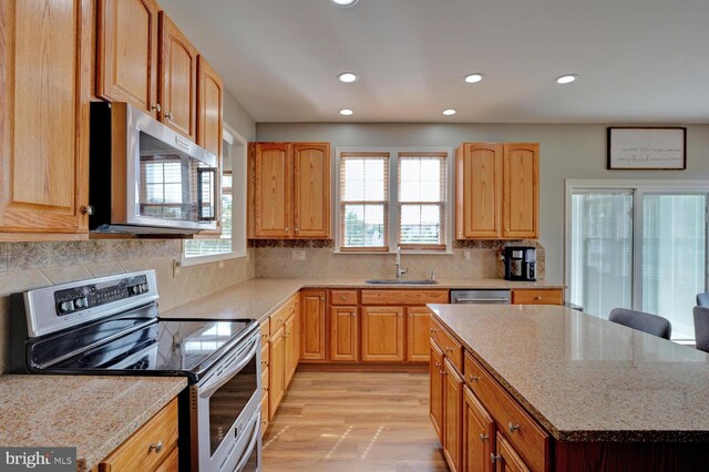 kitchen with light stone countertops, light wood-style floors, appliances with stainless steel finishes, and a sink