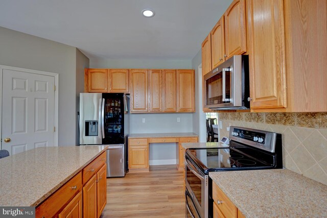 kitchen featuring light wood finished floors, light stone counters, stainless steel appliances, built in desk, and backsplash