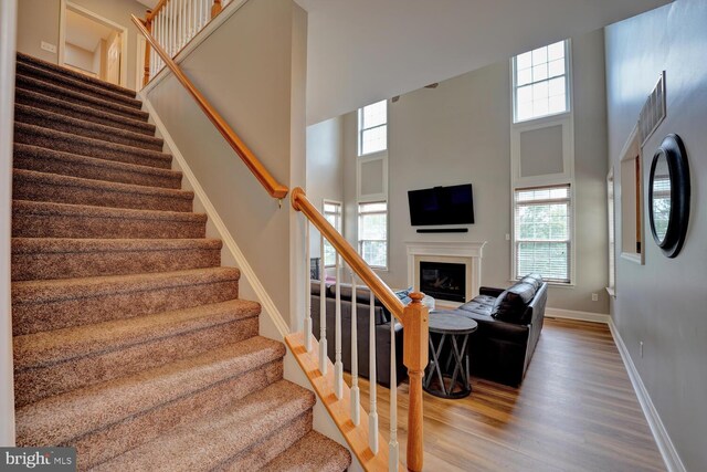 stairs with a glass covered fireplace, a high ceiling, baseboards, and wood finished floors