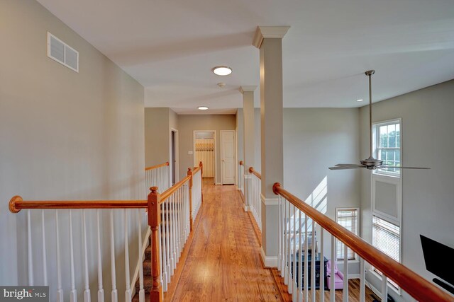 corridor featuring light wood-type flooring, baseboards, visible vents, and an upstairs landing