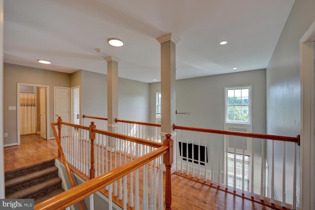 corridor featuring decorative columns, baseboards, wood finished floors, an upstairs landing, and recessed lighting