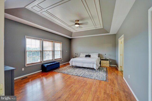 bedroom with a tray ceiling, visible vents, baseboards, and wood finished floors