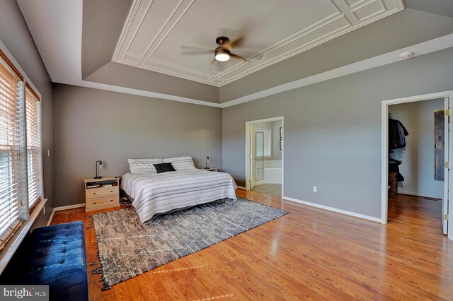 bedroom with connected bathroom, baseboards, a raised ceiling, and wood finished floors