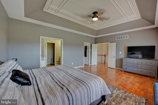 bedroom featuring wood finished floors, visible vents, baseboards, a raised ceiling, and crown molding