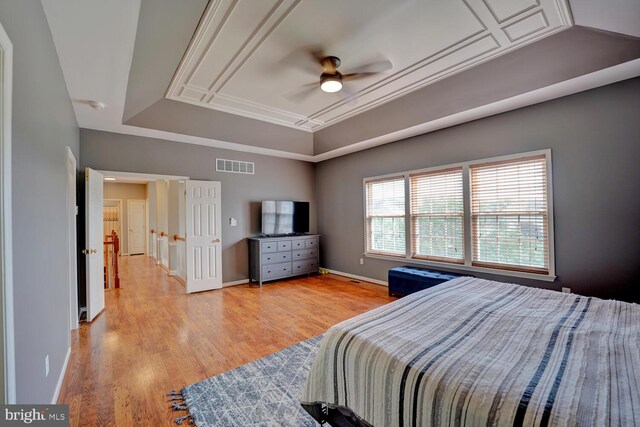 bedroom with wood finished floors, visible vents, baseboards, a raised ceiling, and crown molding