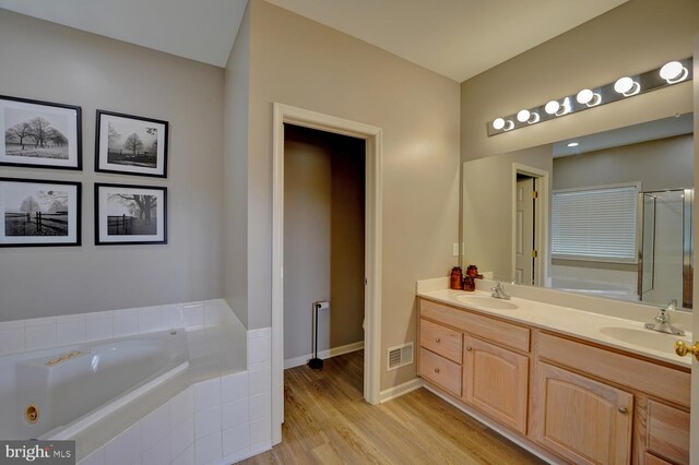 bathroom with a bath, double vanity, a sink, and wood finished floors