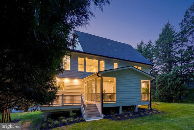 back house at dusk featuring a lawn, a sunroom, and a deck