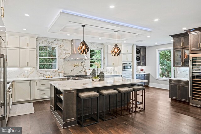 kitchen with a tray ceiling, wall chimney exhaust hood, plenty of natural light, and a center island