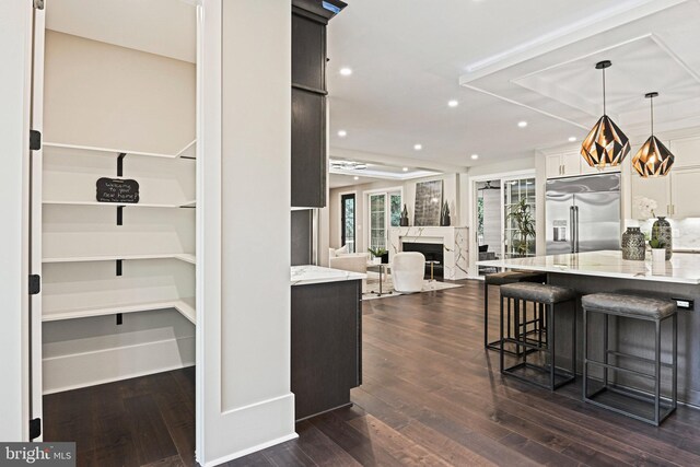 kitchen with a high end fireplace, a kitchen breakfast bar, dark hardwood / wood-style flooring, stainless steel built in refrigerator, and light stone counters