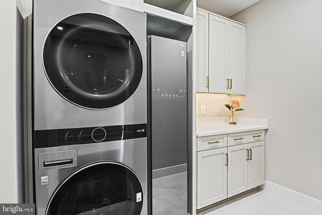 laundry area with stacked washer and clothes dryer, cabinets, and light tile patterned flooring