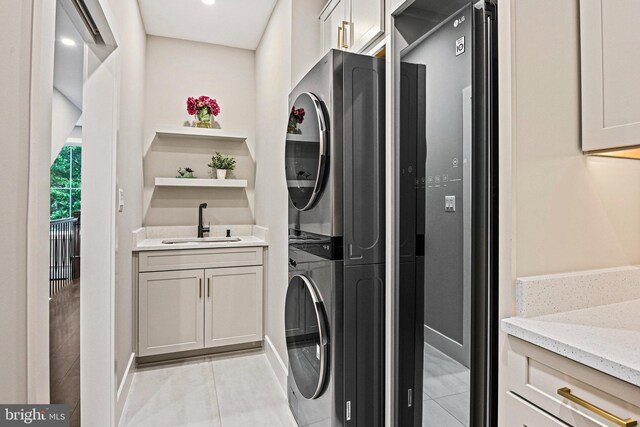 laundry area featuring light tile patterned floors, sink, and stacked washer and dryer