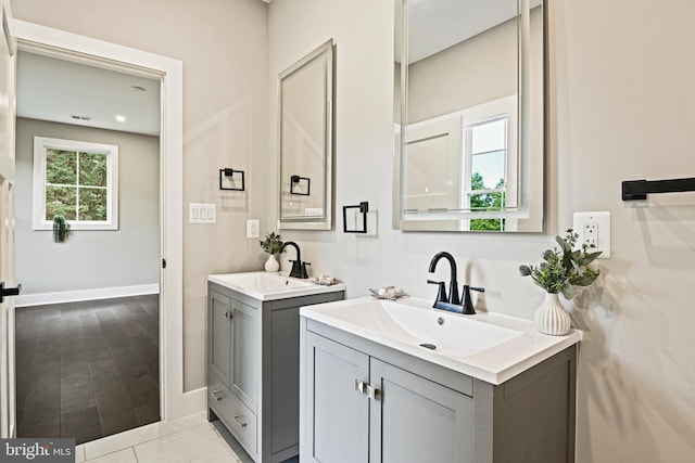 bathroom with wood finished floors, two vanities, a sink, and baseboards