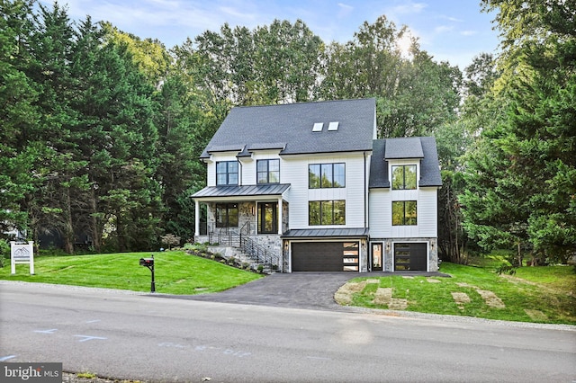 view of front facade with a garage, aphalt driveway, metal roof, a standing seam roof, and a front lawn