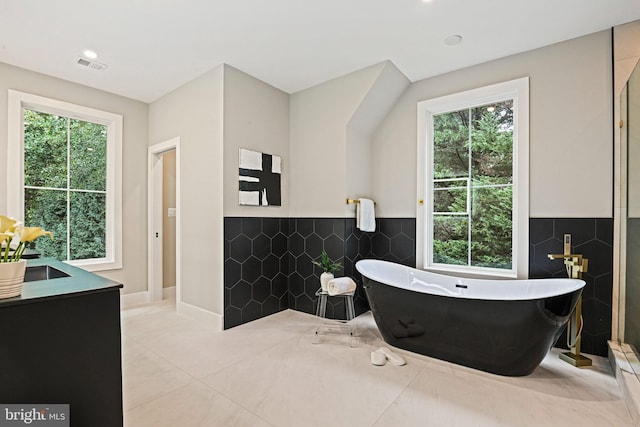 bathroom featuring a soaking tub, visible vents, a sink, and tile walls