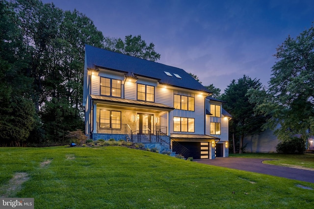 view of front of home featuring driveway, an attached garage, a standing seam roof, a front lawn, and a porch