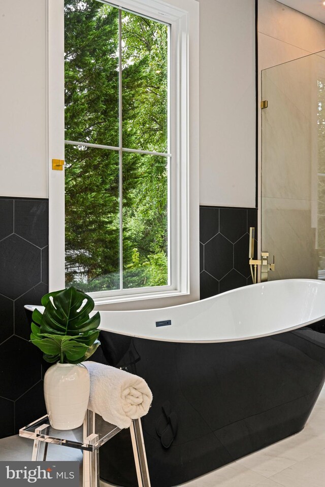 bathroom featuring tile walls, a bathtub, and a healthy amount of sunlight