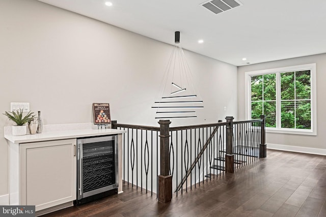 corridor with beverage cooler, visible vents, dark wood finished floors, an upstairs landing, and recessed lighting